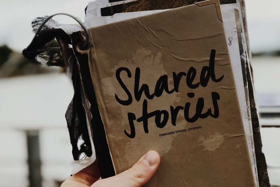 A hand holding up a brown binded book with a covered that reads, "Shared stories."